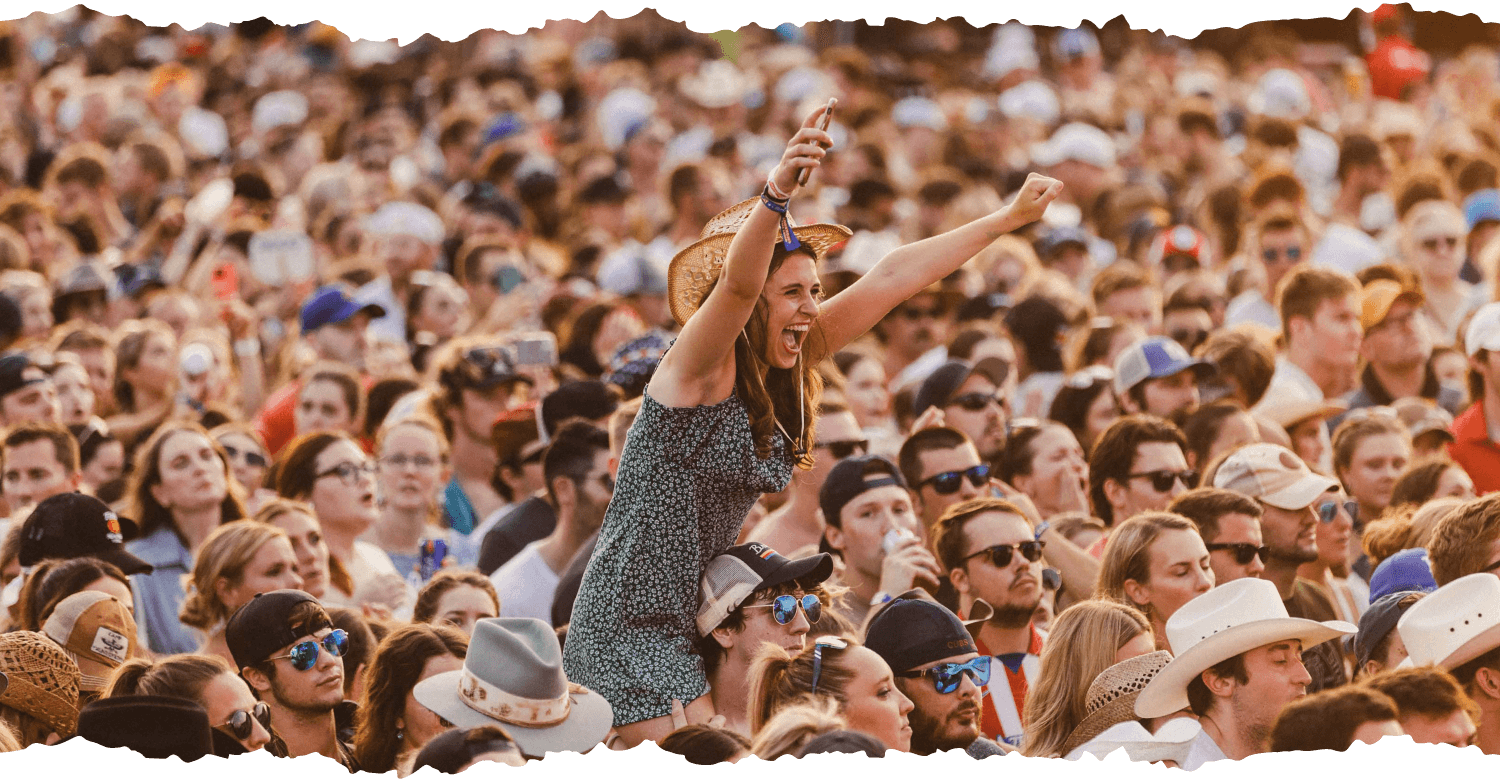 crowd shot focusing on a woman sittig on a mans shoulders so she can see over the crowd