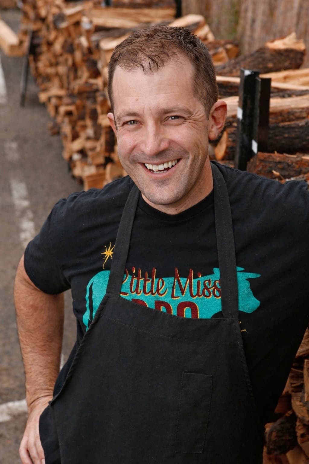 a picture of Scott Holmes of Little Miss BBQ smiling in front of stacks of wood