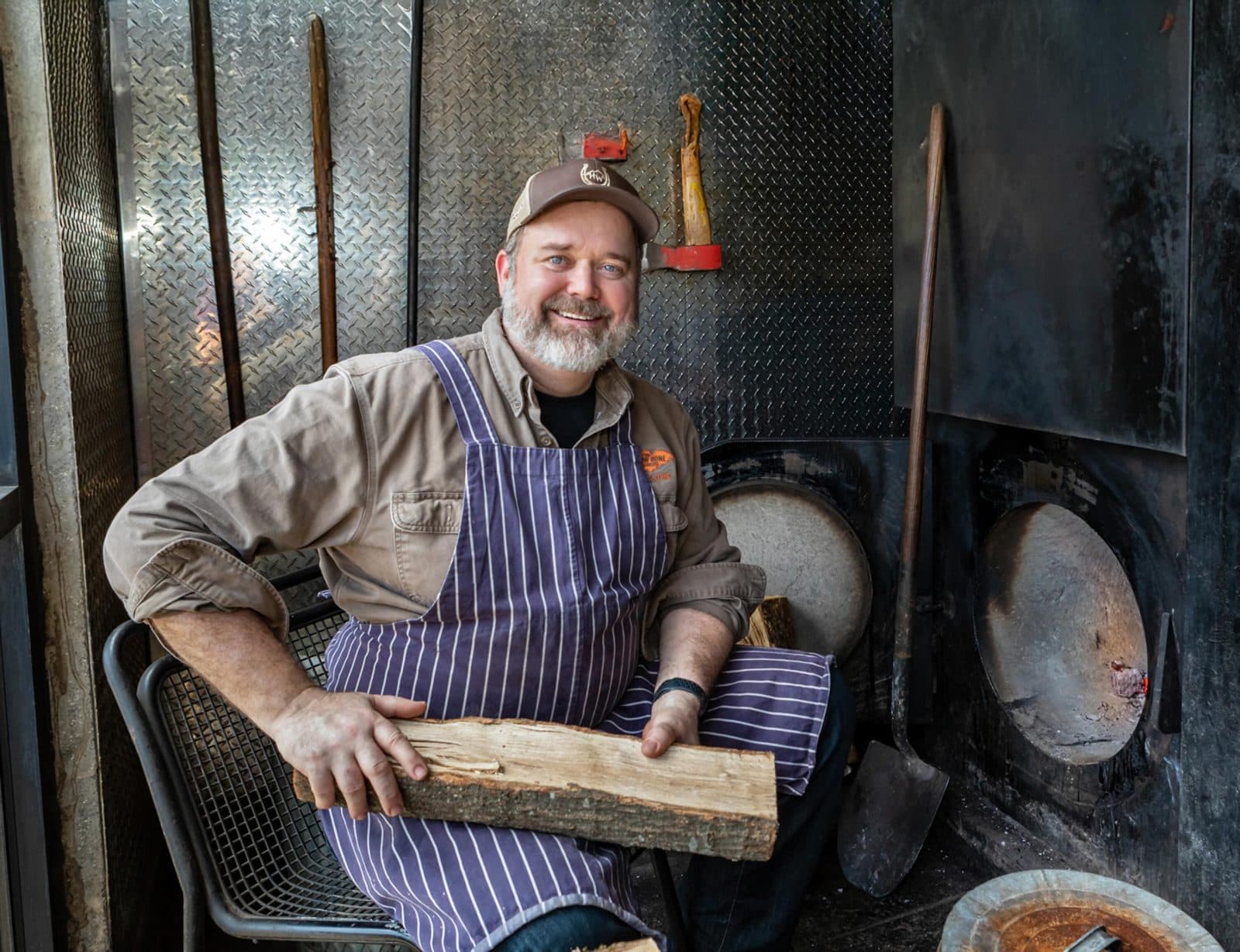 man in front of smoker holding chopped wood